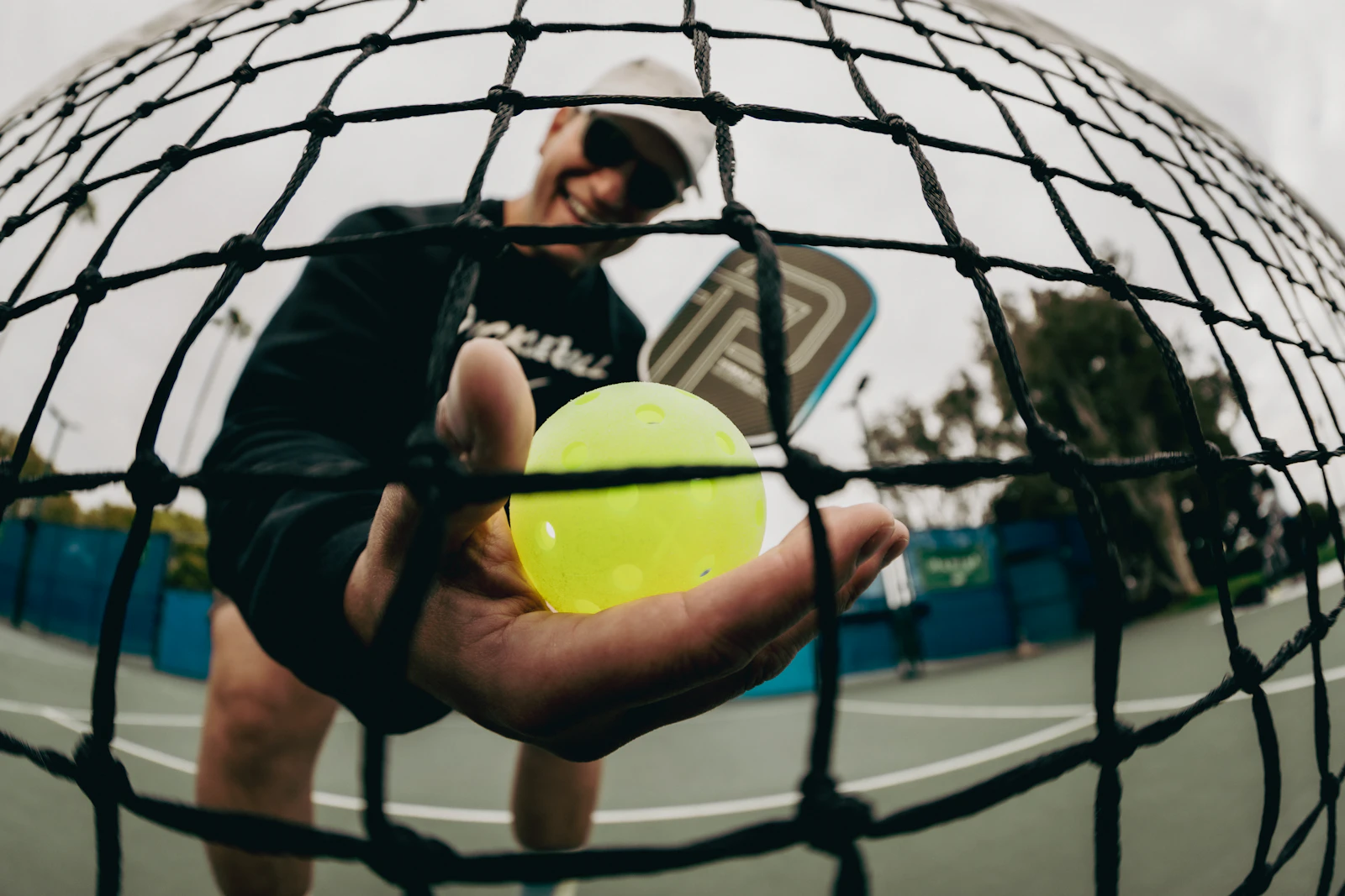 Jugador de pickleball preparado junto a la red con la pelota en la mano